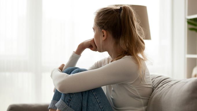 [Translate to French:] Upset woman sitting on couch alone at home