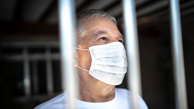 Senior man in isolation at home for virus outbreak looking through window